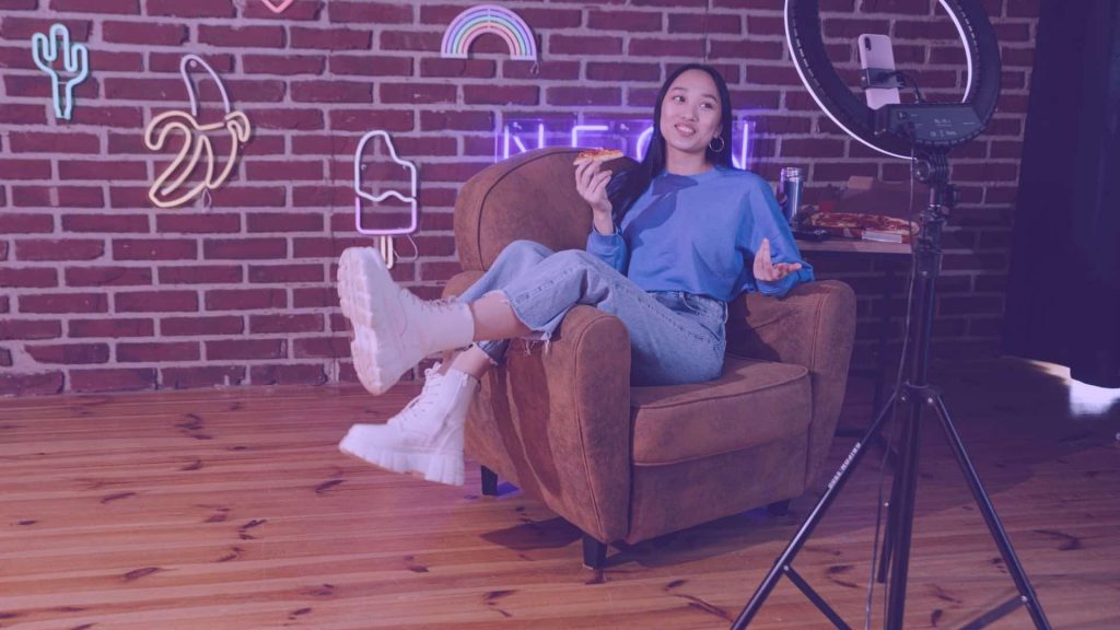 Young girl on a couch recording herself with a phone, main image for the article 'Earning on Twitch: Top 5 Strategies.'