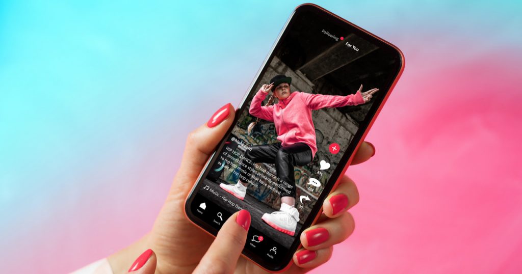 a hand with pink nail polish holding an iPhone that shows a boy break dancing viral TikTok video 