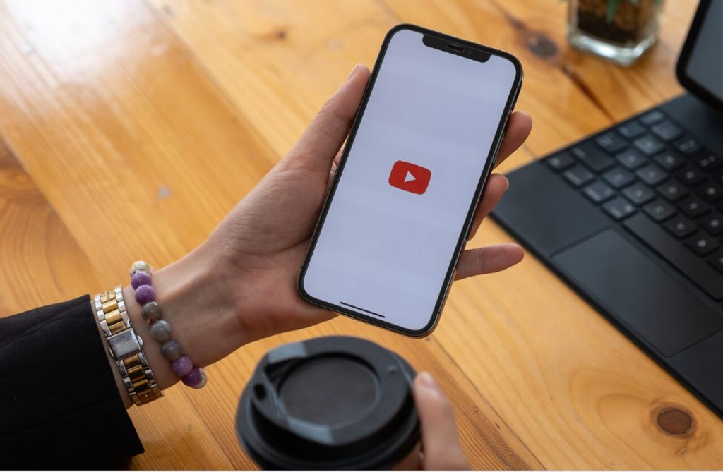 a hand holding a smartphone showing the YouTube app