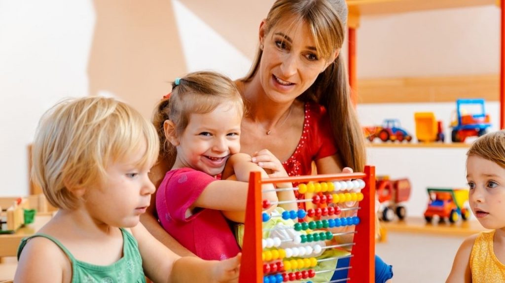 A woman looks at the abacus with three children, one of the children smiles at the camera