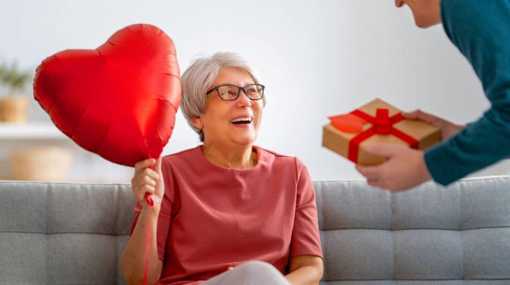 An old woman holding a balloon and a man giving a gift to someone